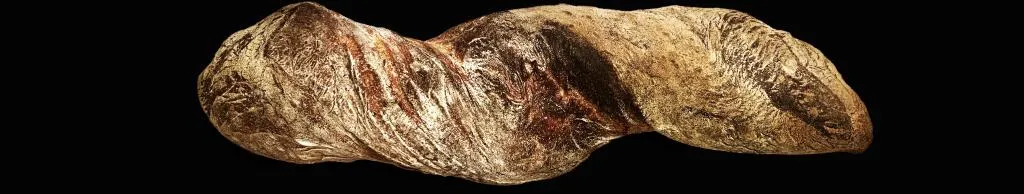 Ein längliches, goldbraunes Baguette mit knuspriger, rissiger Kruste.