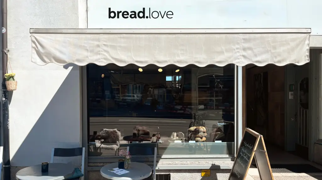 Die Front der Handwerksbäckerei bread.love mit Brotauslage im Schaufenster und gemütlichen Sitzgelegenheiten im Außenbereich.
